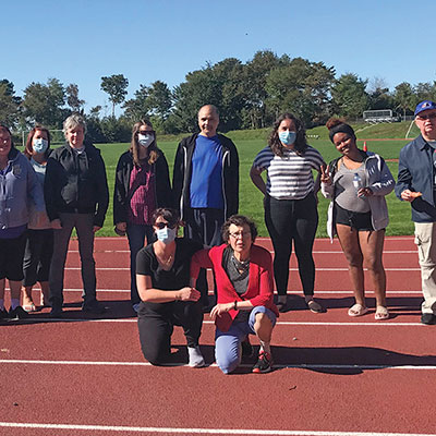 Ten people standing and kneeling on an outside track on a sunny day.
