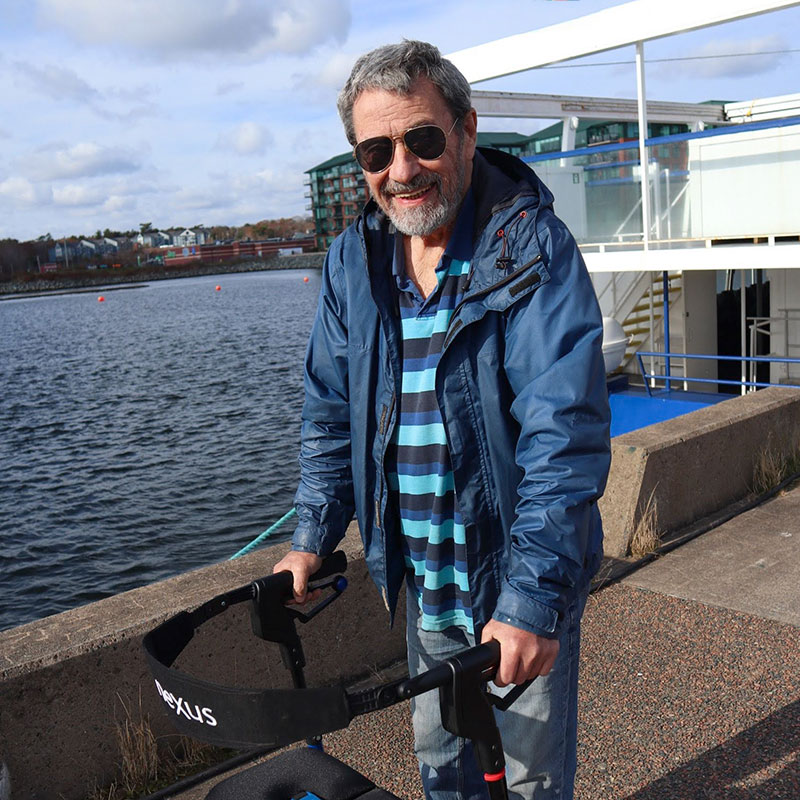 Man using a walker, standing in the sun near an urban waterfront.