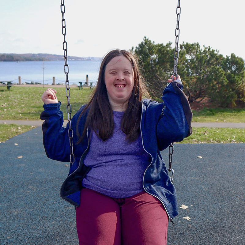 Young woman sitting outside on a swing and smiling into the sunshine.